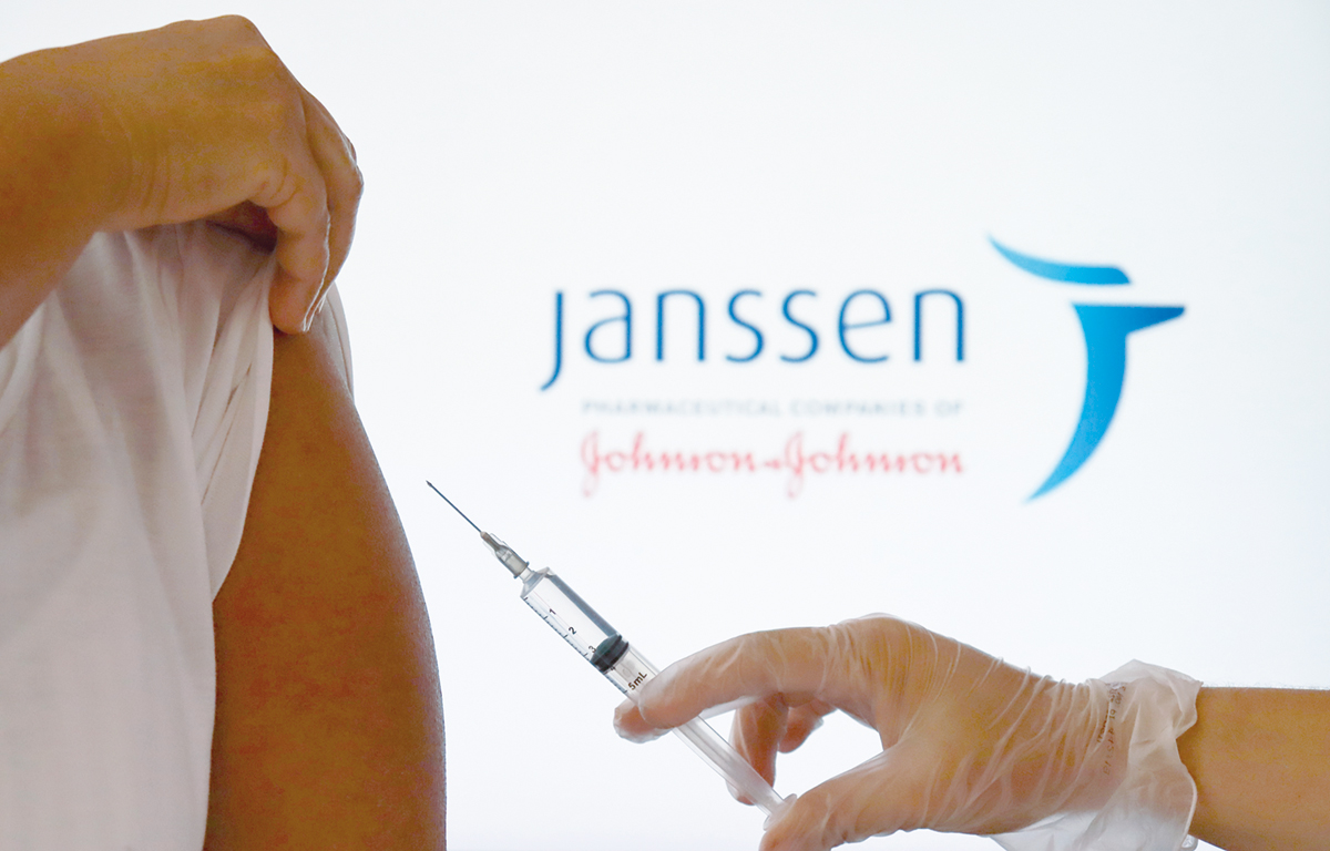 Bahia, Brazil – December 23, 2020. Hand holding a syringe against woman’s shoulder, with Janssen by Johnson and Johnson logo displayed in the background. Covid-19 vaccine concept.