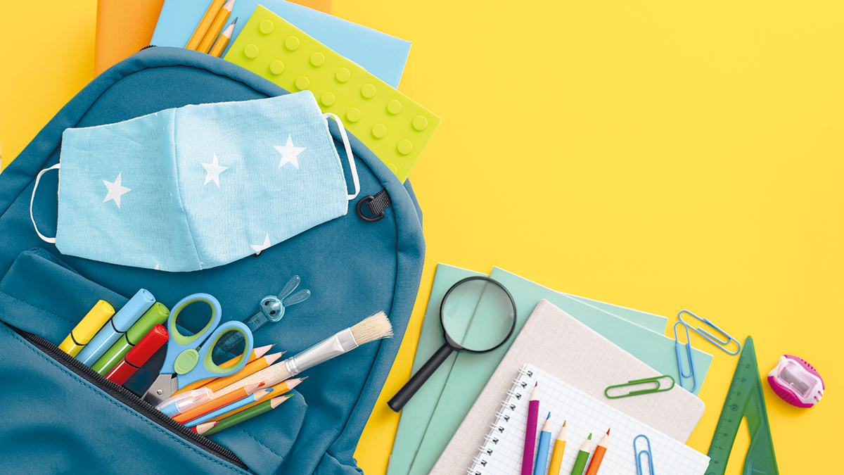 School supplies, blue backpack medical mask yellow background. Back to school, pandemic coronavirus concept, flat lay.Horizontal. Selective focus. View from above. Copy space.