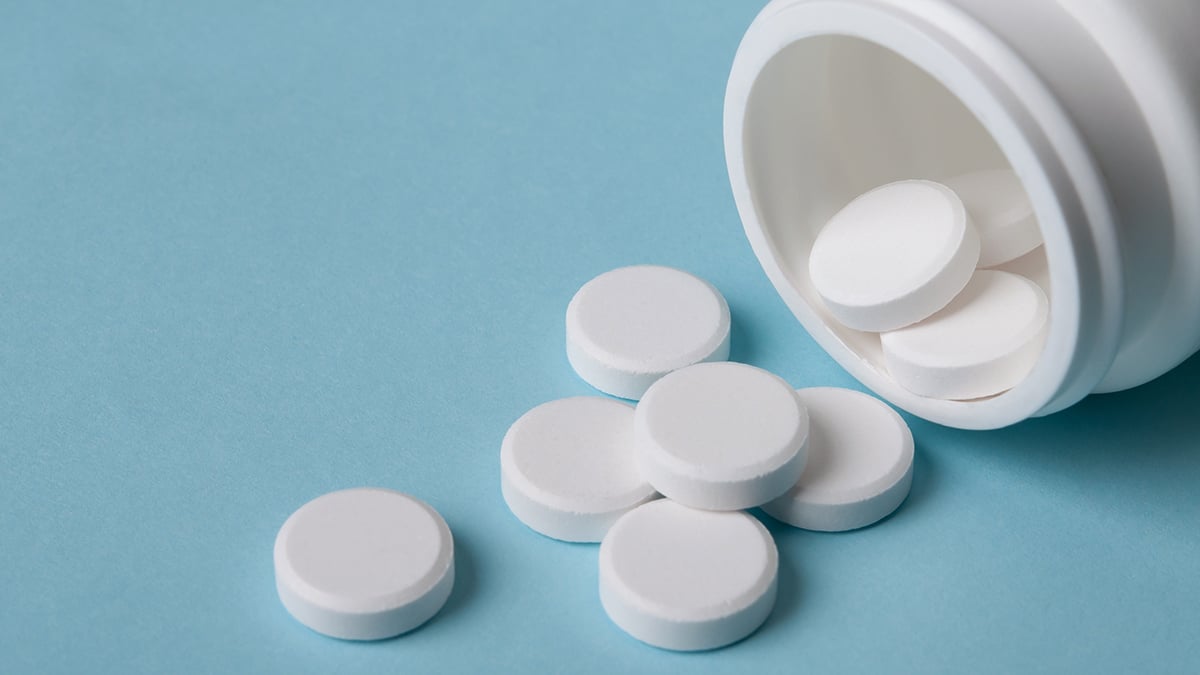 white round pills pouring out of the medicine bottle on blue background with copy space; medical care concept