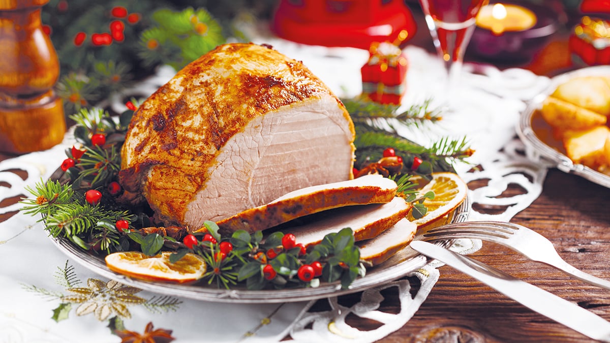 Christmas baked ham, served on the old plate. Spruce twigs all around. Front view.