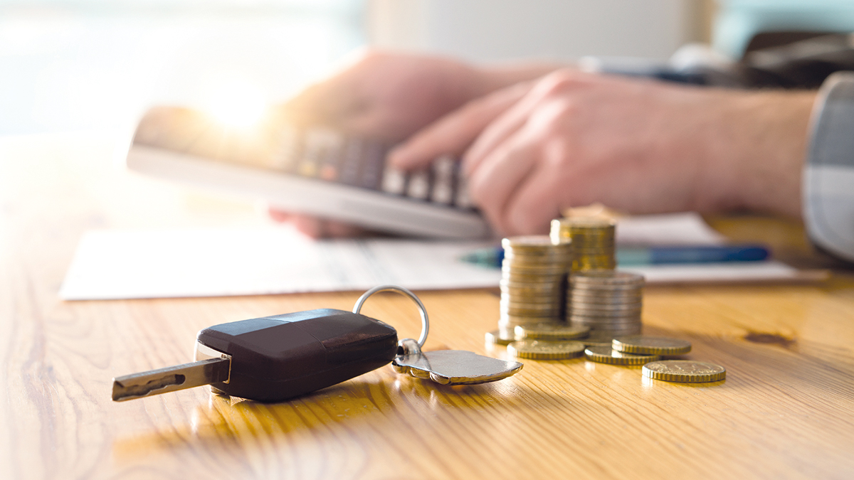 Car keys and money on table with man using calculator. Buyer counting savings and gas cost or salesman calculating sales price, vehicle value or road taxes.