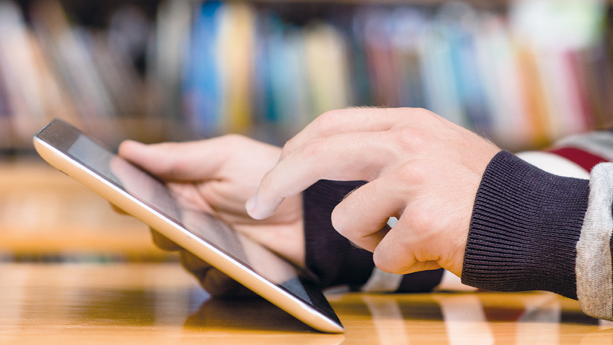 Hands typing on tablet computer in library