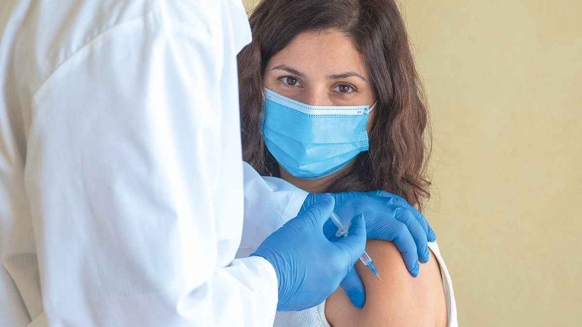 Doctor making a vaccine to a brunette girl in the shoulder. Woman looking at the camera.